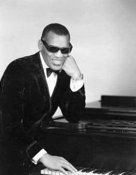 Photo of famous blind pianist Ray Charles sitting next to a piano.