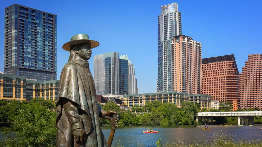 Stevie Ray Vaughan Statue In Front Of Downtown Austin, Texas And Colorado River