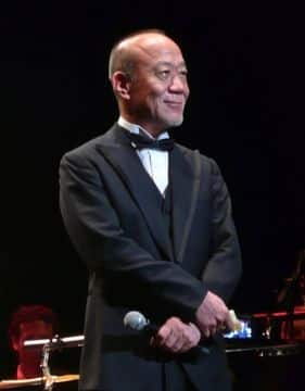 Photo of Studio Ghible composer Joe Hisaishi holding a microphone on stage
