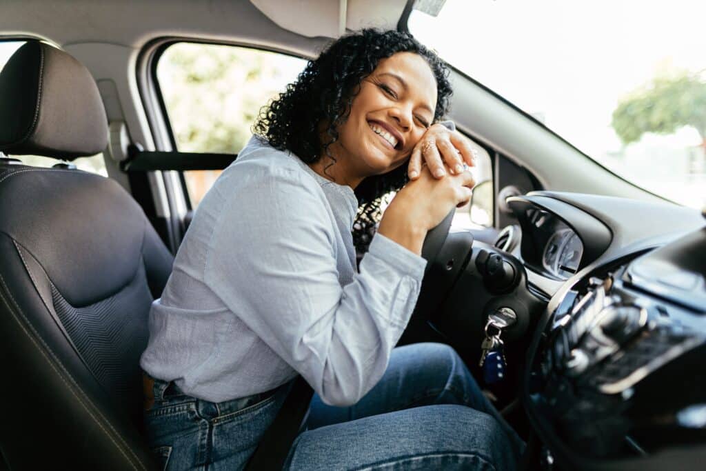 Young And Cheerful Woman Enjoying New Car Hugging Steering Wheel